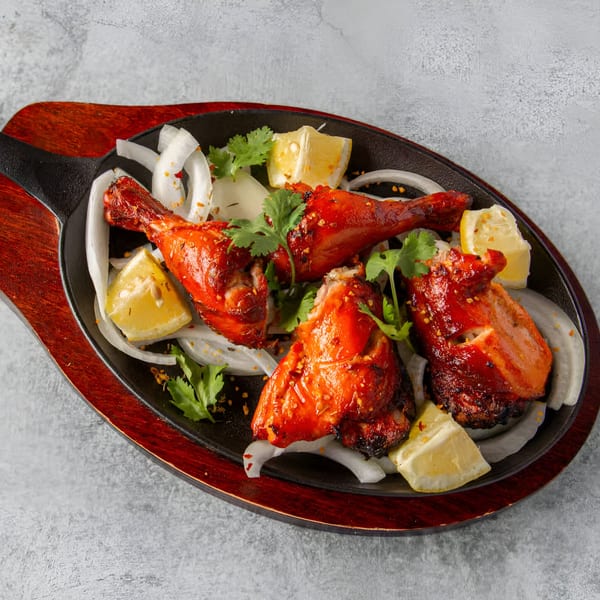 Tandoori chicken drumsticks with sliced onions, lemon wedges, and cilantro on a sizzling platter.