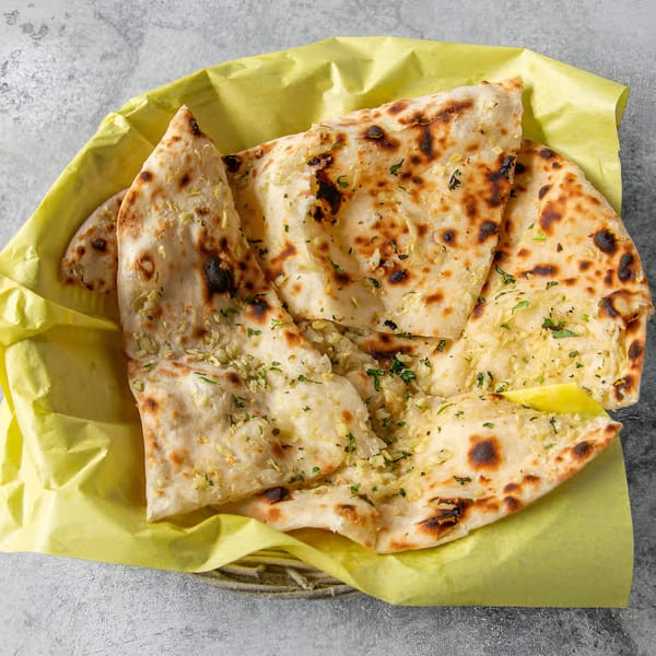 Garlic naan bread from India House, served in a yellow paper-lined basket.