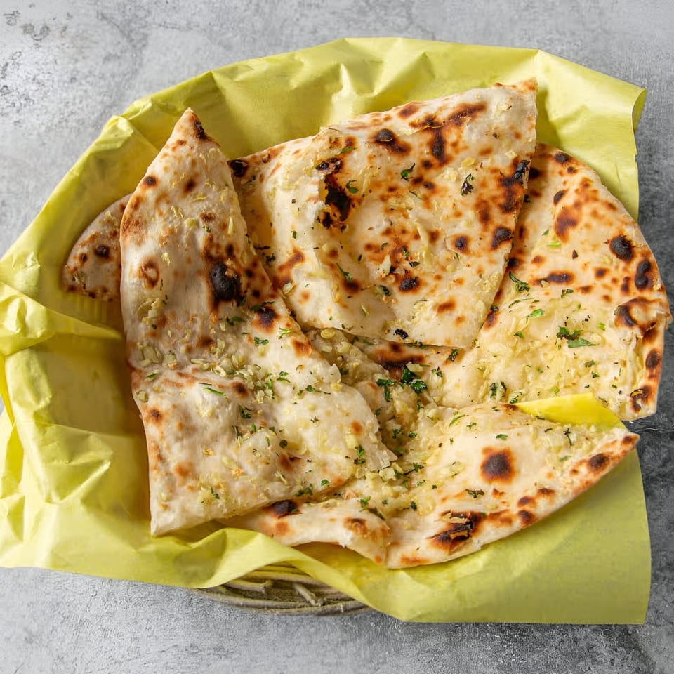 Garlic naan bread from India House, served in a yellow paper-lined basket.