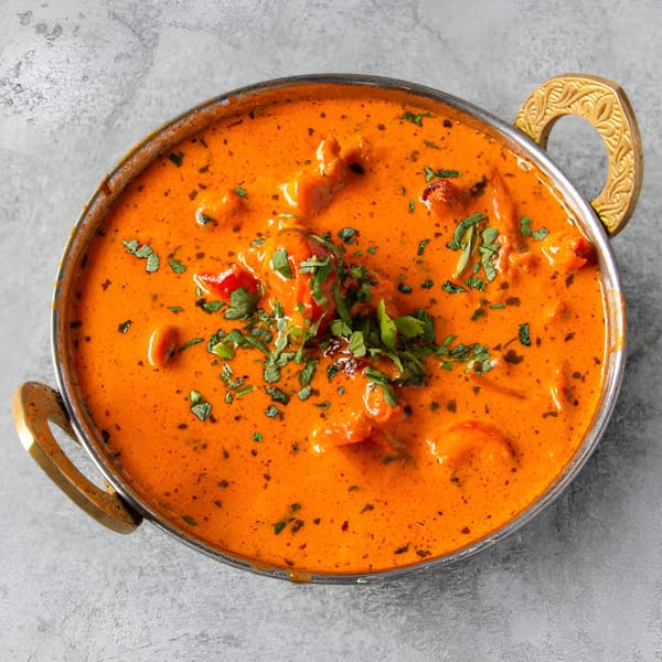 A vibrant orange Indian curry, garnished with fresh green herbs, served in a traditional metal karahi.