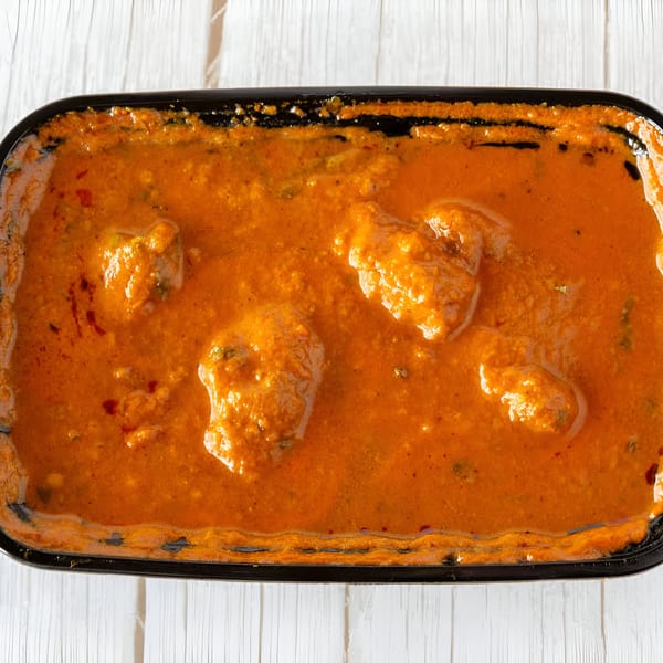 Close-up of Indian butter chicken in a black serving dish on a white wooden surface.