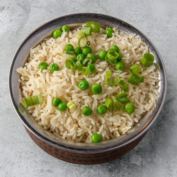 A metal bowl of Indian House basmati rice with green peas and chopped scallions.