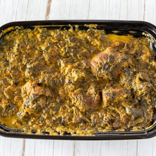 Close-up of a black container filled with a rich, green Indian curry with chunks of meat.